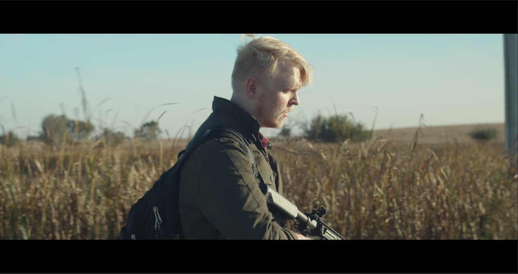 Man walking a gravel road, carrying a gun