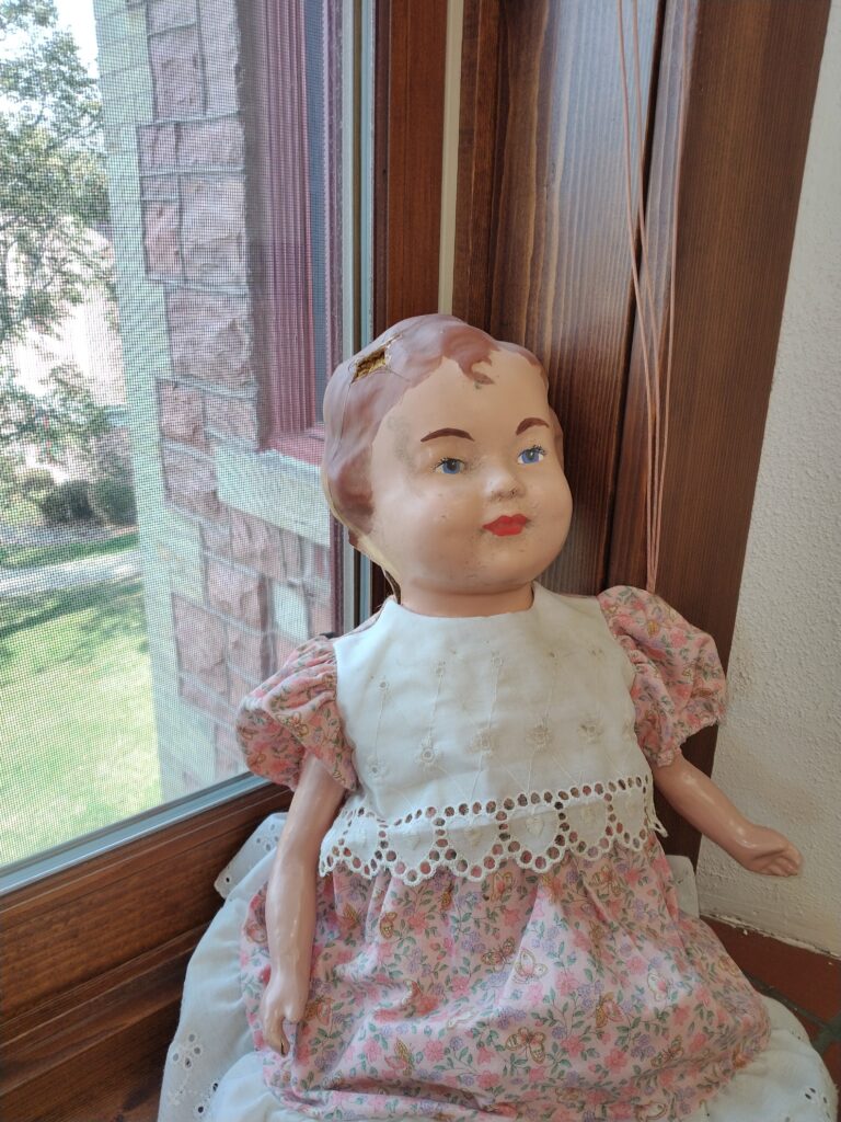 Creepy doll sitting on window sill.